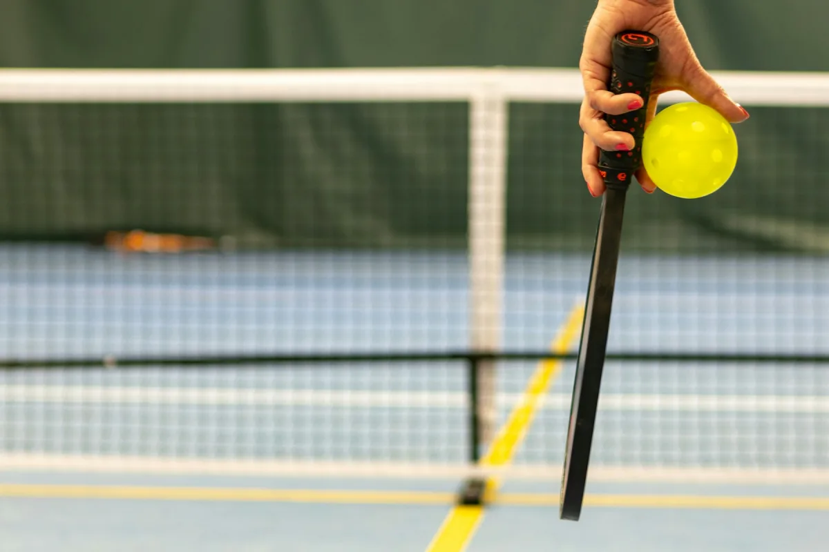 A player holds a pickleball paddle and yellow ball beside the net