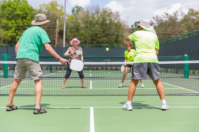 Four older adults playing doubles pickleball outdoors at The Villages